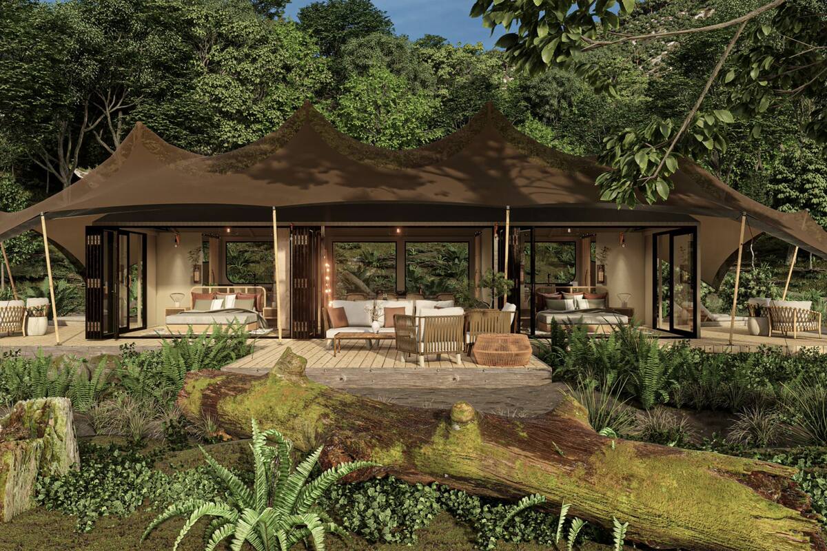 A luxurious outdoor pavilion with a bed, seating area, and a view of the surrounding forest.
