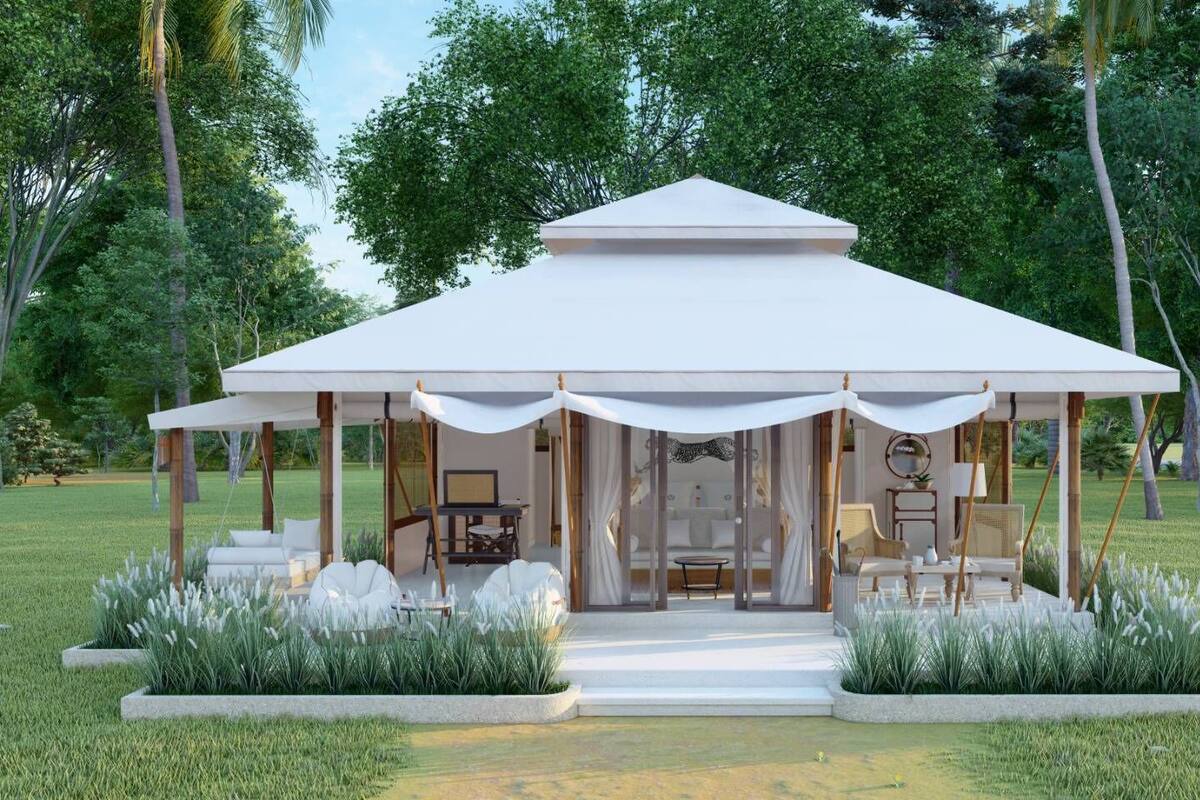 A modern pavilion with a white roof and open sides, surrounded by lush greenery and a well-maintained lawn.