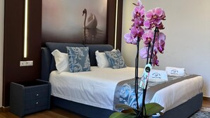 A modern bedroom with a large bed, a bedside table, a round wooden table with a vase of flowers, and a wall-mounted light fixture. - Hotel white swan (Wormeldange)