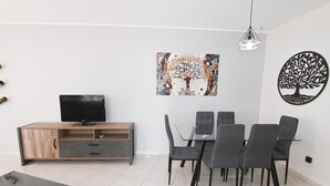 Ein modernes Wohnzimmer mit Fernseher, Esstisch und Stühlen.