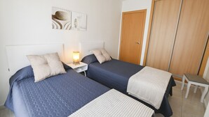 Ein Schlafzimmer mit zwei Betten, einem Nachttisch mit Lampe, einem Holzschrank und einem kleinen Tisch.