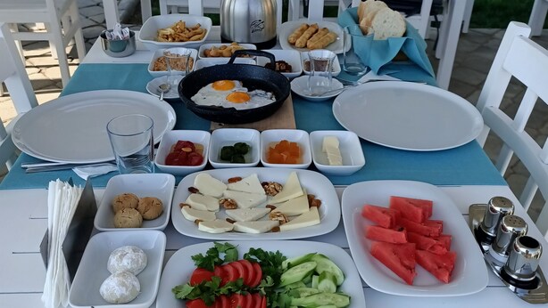 An outdoor dining setup with a variety of dishes, including eggs, nuts, and vegetables, on a table with white chairs and a blue tablecloth. - Rota Bozcaada (Bozcaada)