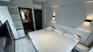 A modern hotel room with a large bed, bedside tables, a wardrobe, and a bathroom visible through an open door. - Rota Bozcaada (Bozcaada)