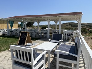 Un área de patio al aire libre con mobiliario blanco, una pérgola y un letrero en una pizarra.