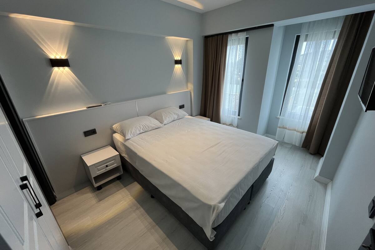 A modern hotel room with a large bed, bedside tables, and wall-mounted lighting.