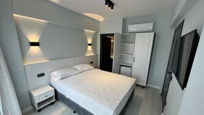 A modern bedroom with a bed, bedside tables, built-in wardrobe, and a wall-mounted TV. - Rota Bozcaada (Bozcaada)