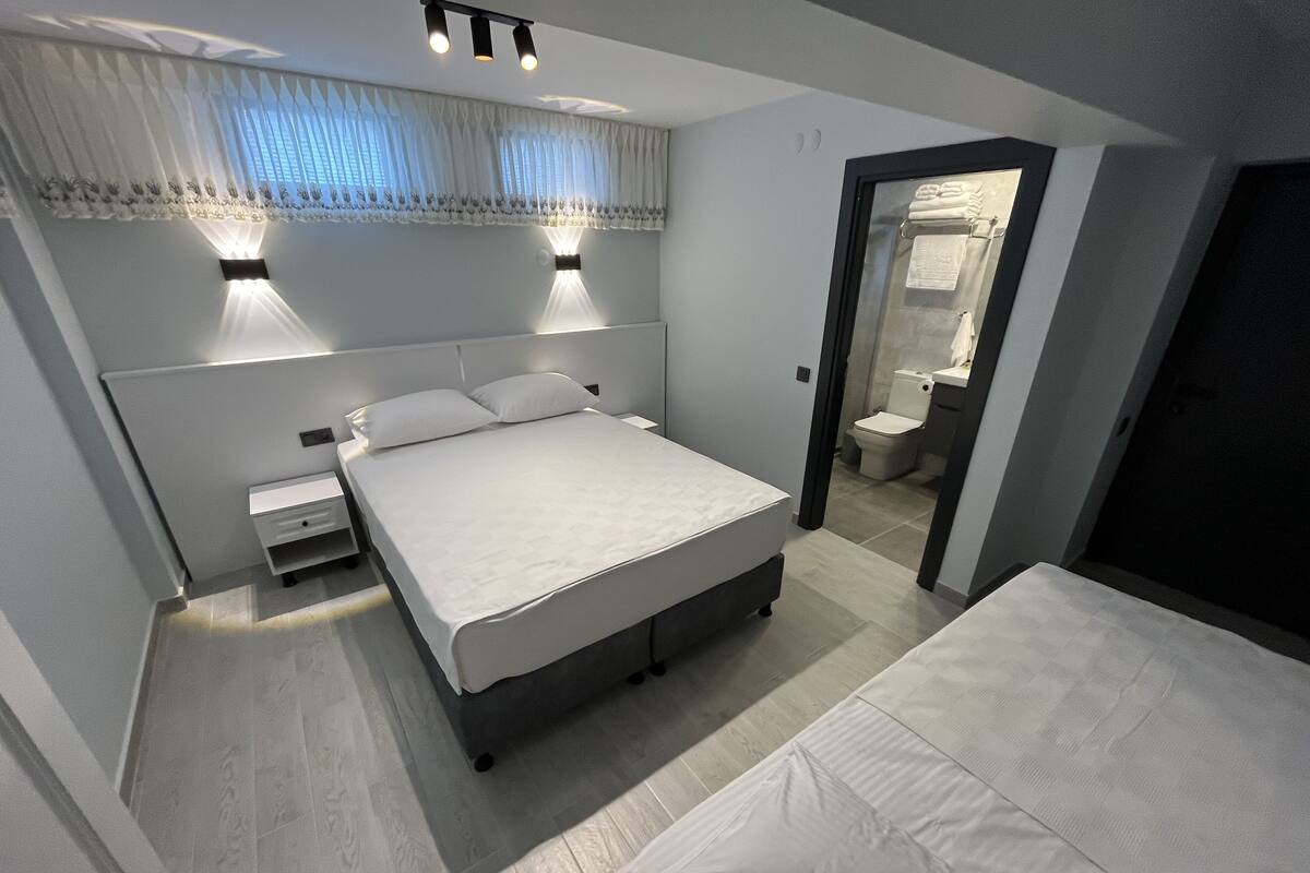 A modern bedroom with a large bed, bedside tables, a wardrobe, and a bathroom visible through an open door.