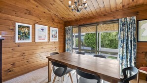 Una habitación con paneles de madera, una mesa grande y sillas, carteles enmarcados en la pared y vistas a la vegetación exterior.