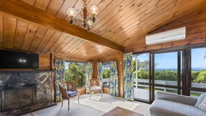 Interior acogedor de una cabaña con chimenea de piedra, techo de madera y un ventanal con vistas panorámicas.