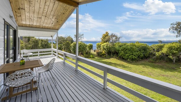Una terraza de madera con una mesa y sillas, con vistas a un exuberante jardín y al mar.