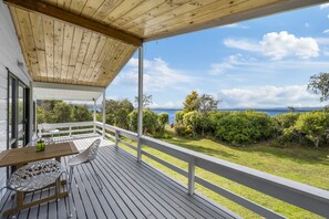 Eine Holzterrasse mit Tisch und Stühlen, mit Blick auf einen üppigen Garten und das Meer.