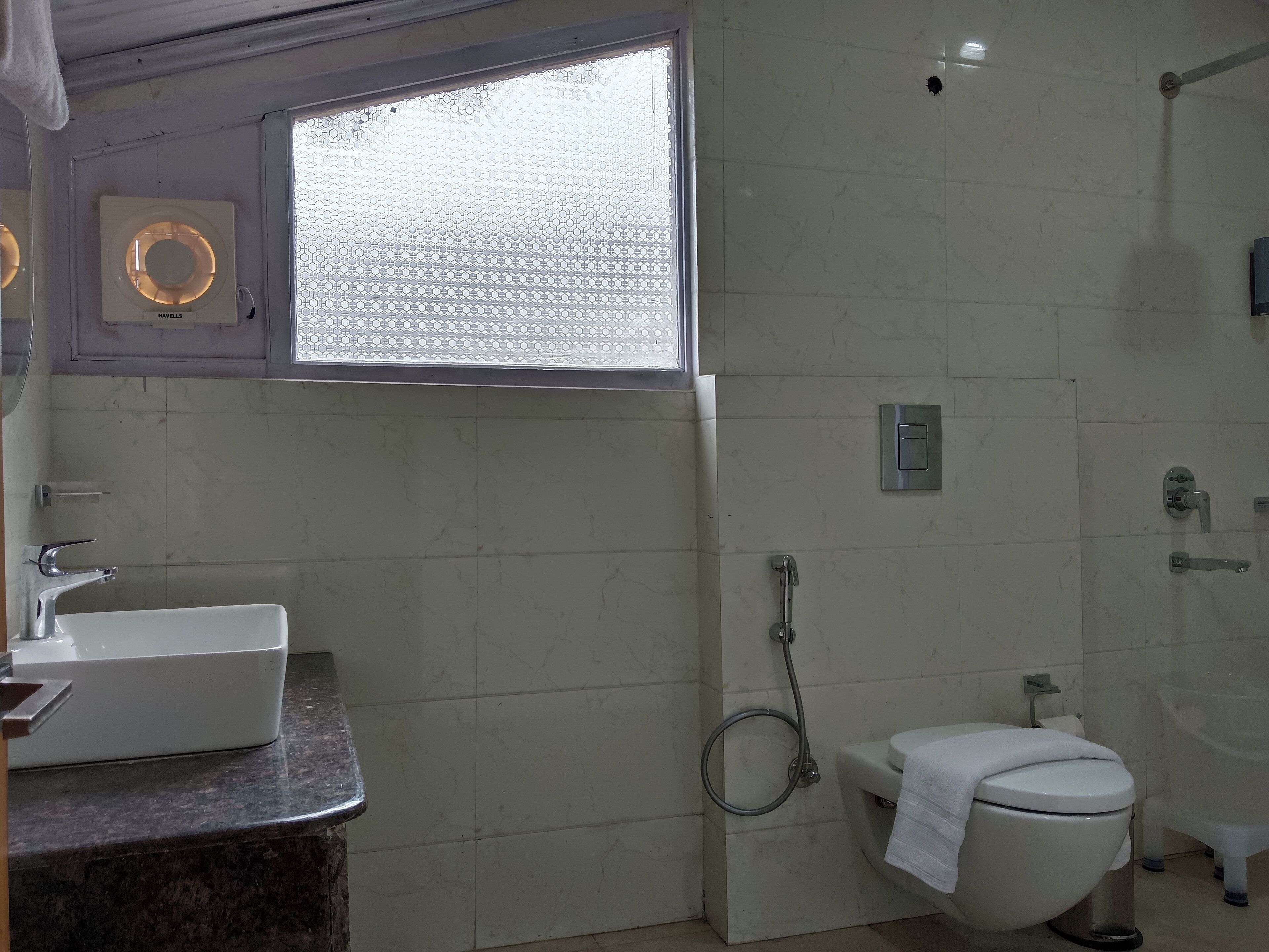 A bathroom with a white sink, toilet, and bathtub. There is a window with a hexagonal pattern, and a towel rack is visible.