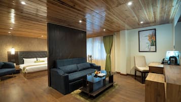 A modern hotel room with a wooden ceiling, a large bed, a dark sofa, a coffee table, and a desk with a lamp.