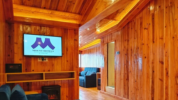 Ein gemütlicher Raum mit Holzwänden, einem Flachbildfernseher mit dem Mount Hotels Logo, einem Kamin und einer komfortablen Sitzecke.