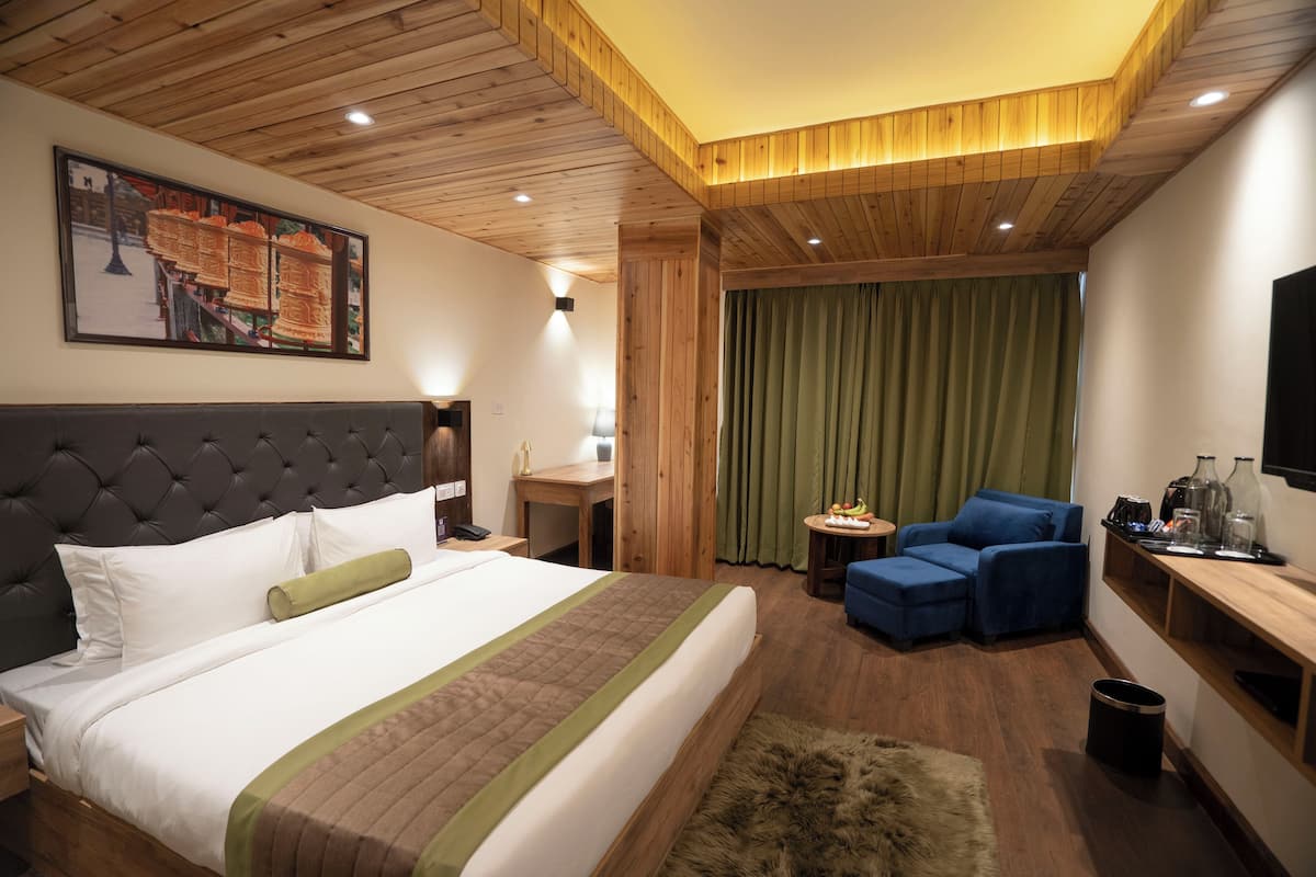 A hotel room with a large bed, a wooden ceiling, a green curtain, a blue sofa, and a television on the wall.