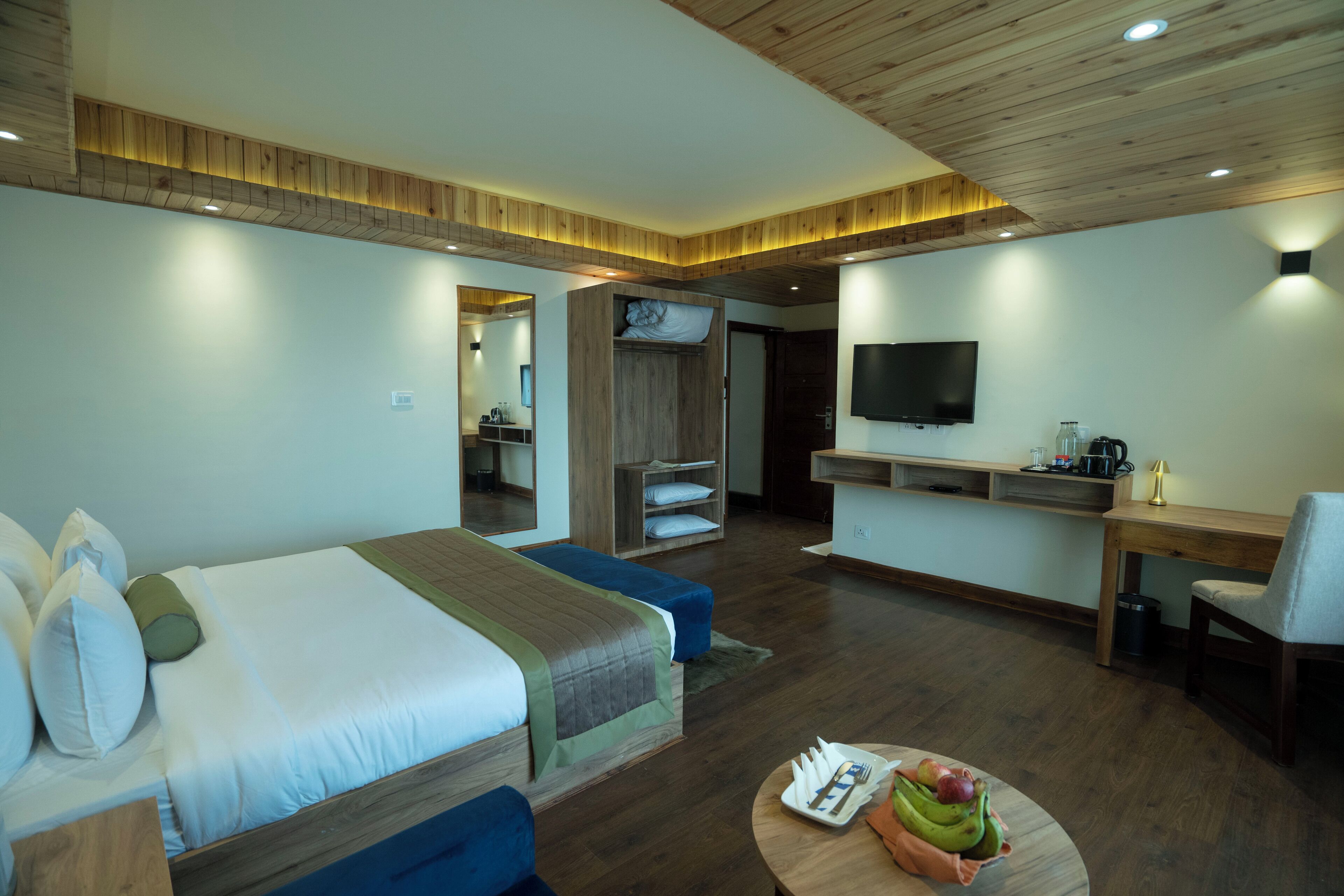 A modern hotel room with a large bed, a desk, a TV, and a kitchenette.