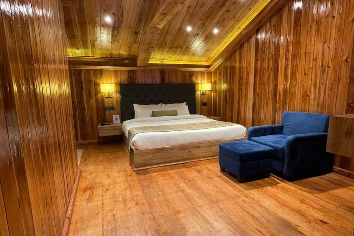 A wooden-paneled room with a bed, a blue armchair, and a nightstand with a lamp.