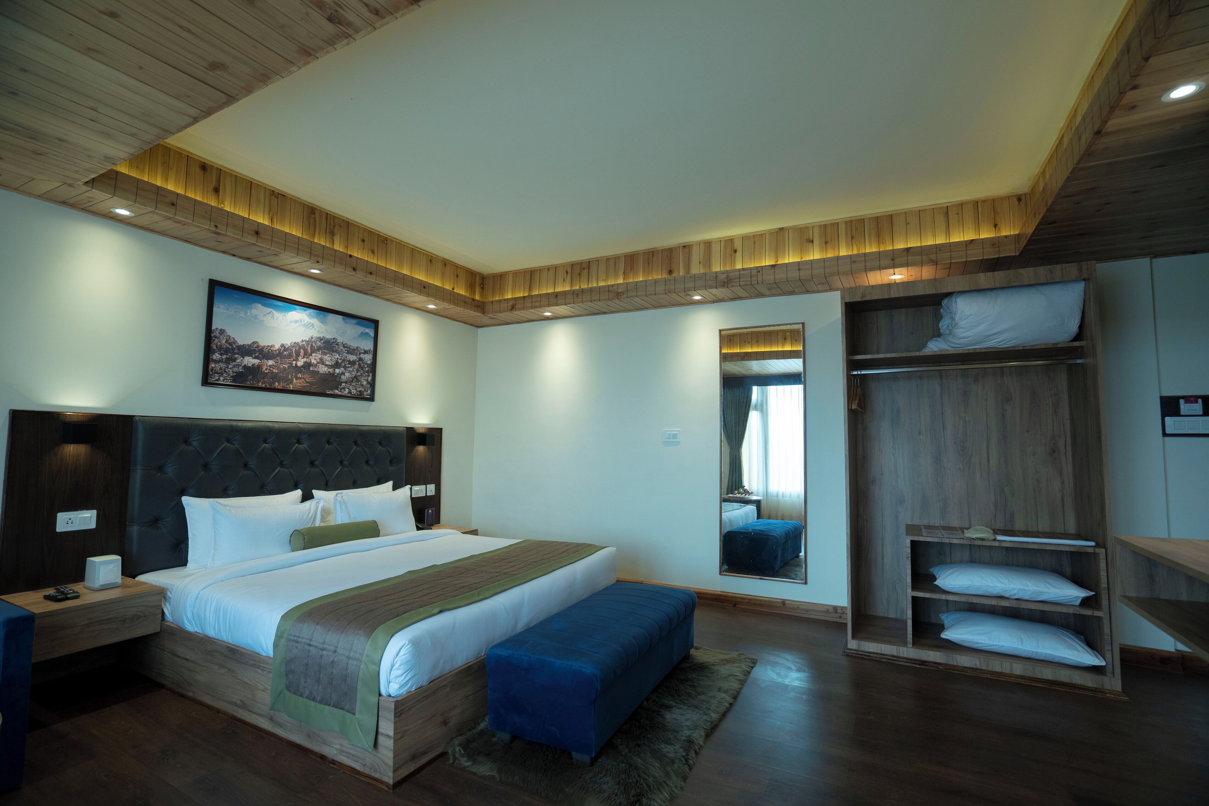 A modern bedroom with a large bed, wooden headboard, bedside tables, a bench, a wardrobe, and a mirror.