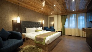 Ein modernes Schlafzimmer mit Holzbalkendecke, einem großen Bett mit grün-weiß gestreifter Bettdecke, einem dunkelblauen Sessel, einem kleinen runden Teppich und einem Nachttisch mit Lampe.