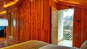 Ein Zimmer mit Holzboden, einem Bett, einer zur Außenwelt führenden Tür und Blick auf Gebäude.