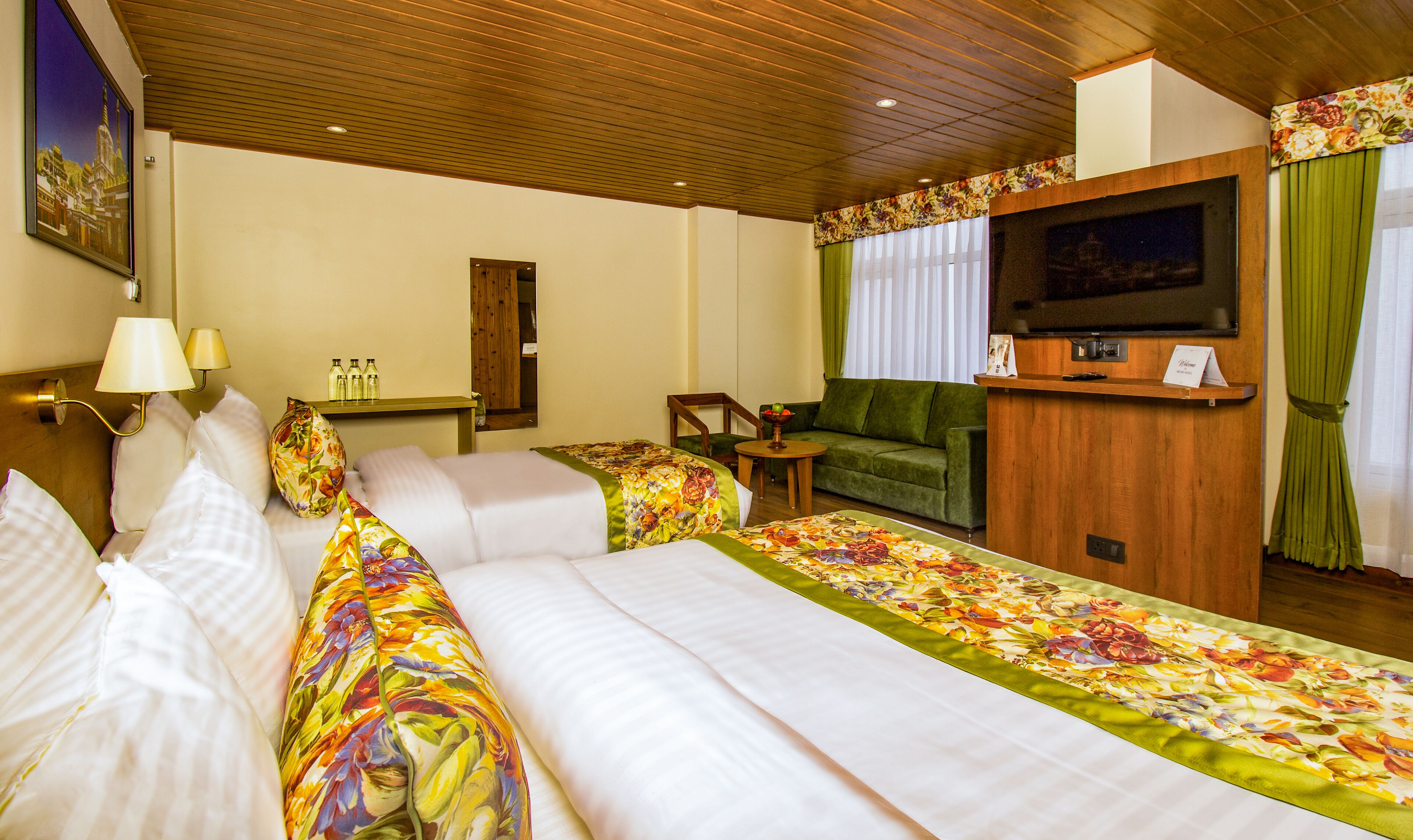 A hotel room with two beds, a sofa, a television, and a small table.
