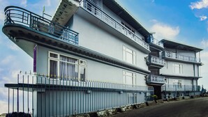 Un edificio de dos pisos con balcones, techo plano y una valla metálica.