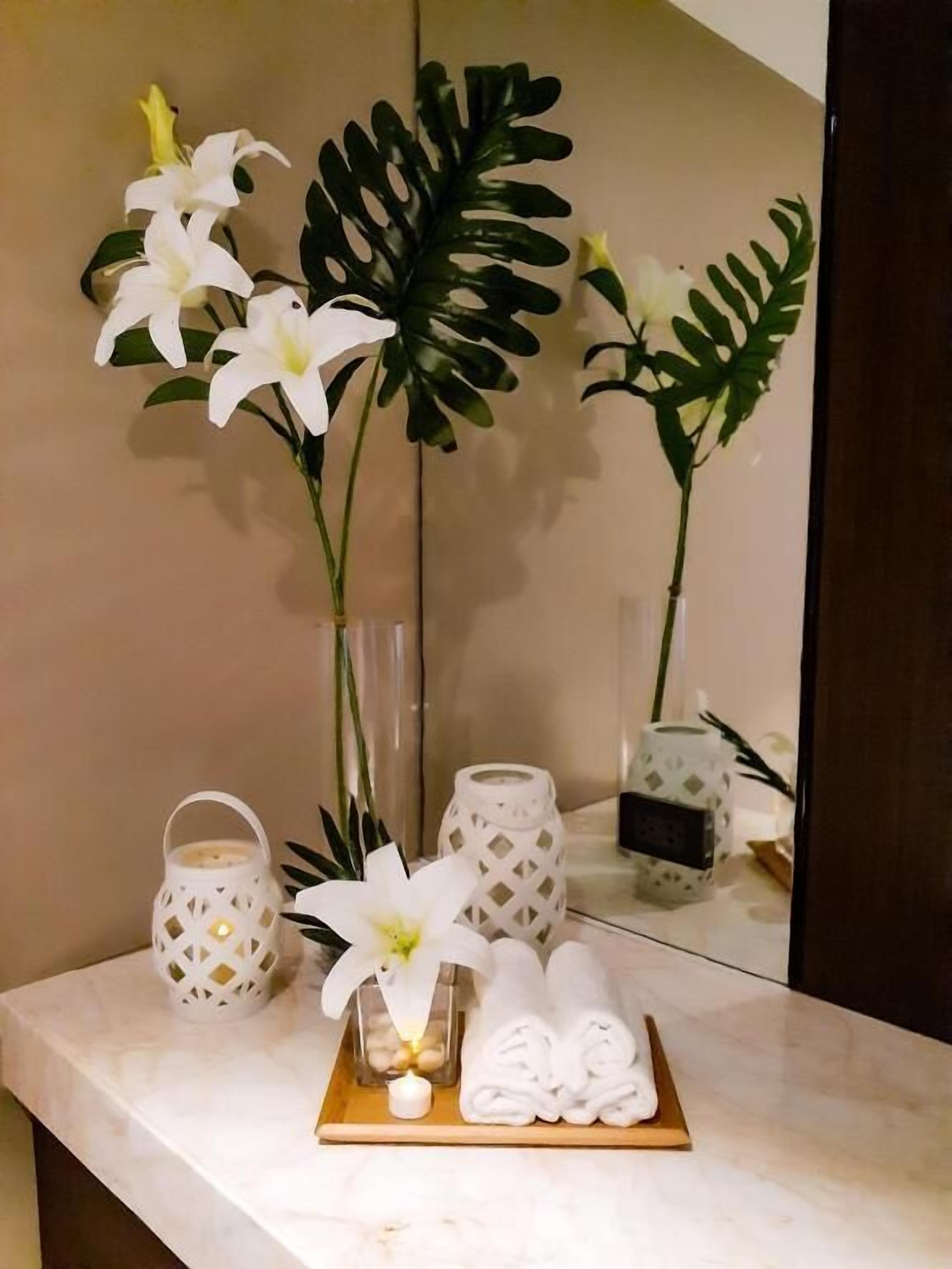 A bathroom vanity with a mirror, white towels, a small candle, and decorative plants.