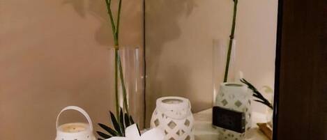 Un tocador de baño con espejo, toallas blancas, una vela pequeña y plantas decorativas.