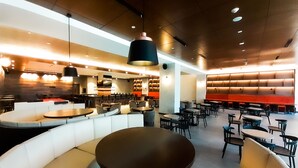 Un restaurante espacioso con techos altos, iluminación moderna y diversas opciones de asientos, incluyendo cabinas y mesas.