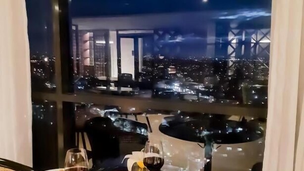 Una mesa de comedor con platos, copas de vino y cestas, con vista a un paisaje urbano nocturno.