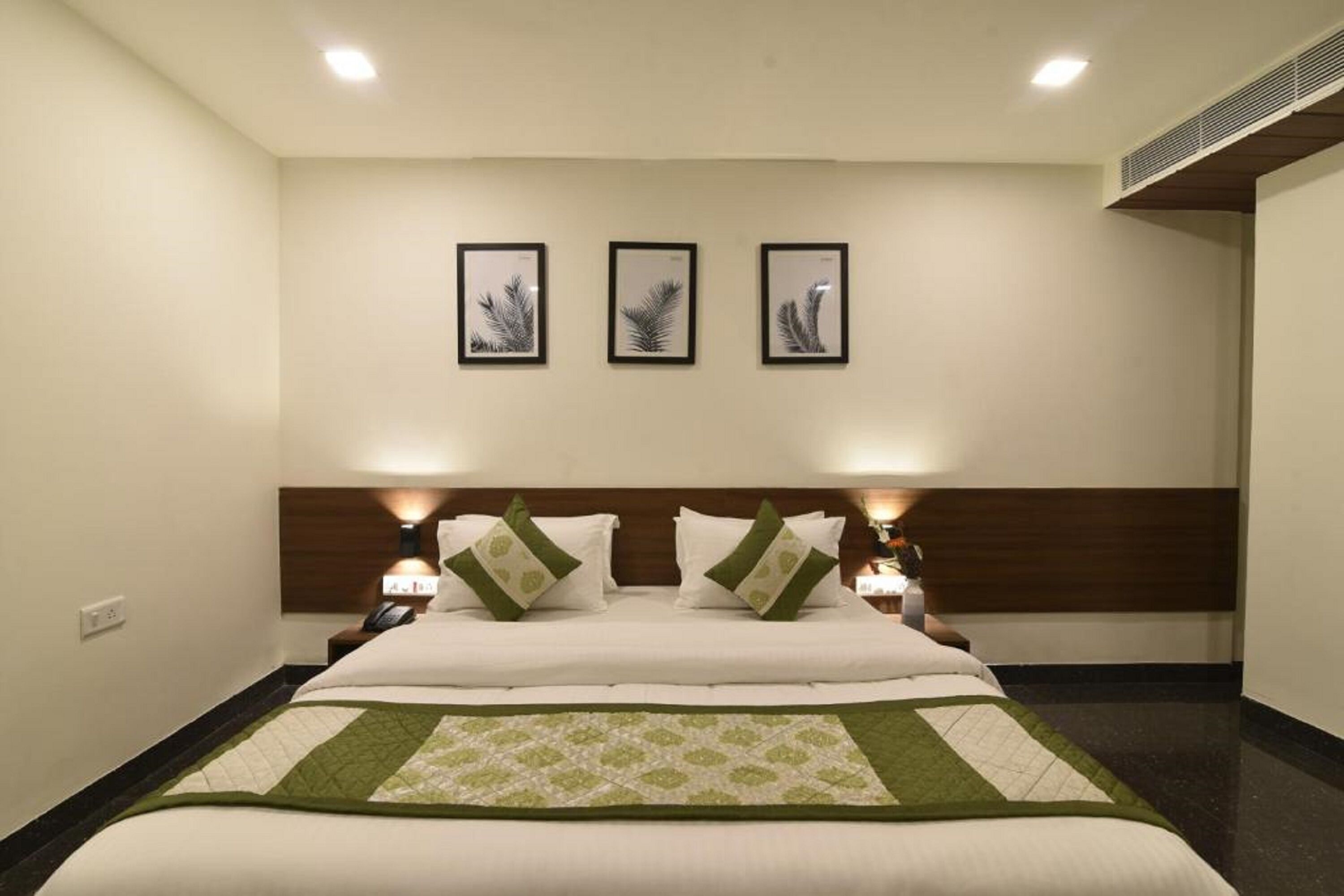 Une chambre d’hôtel avec un grand lit, deux tables de chevet et trois œuvres d’art encadrées accrochées au mur.