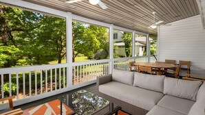 Eine überdachte Terrasse mit einer Couch, einem Esstisch und Stühlen, mit Blick auf eine üppige, grüne Landschaft.