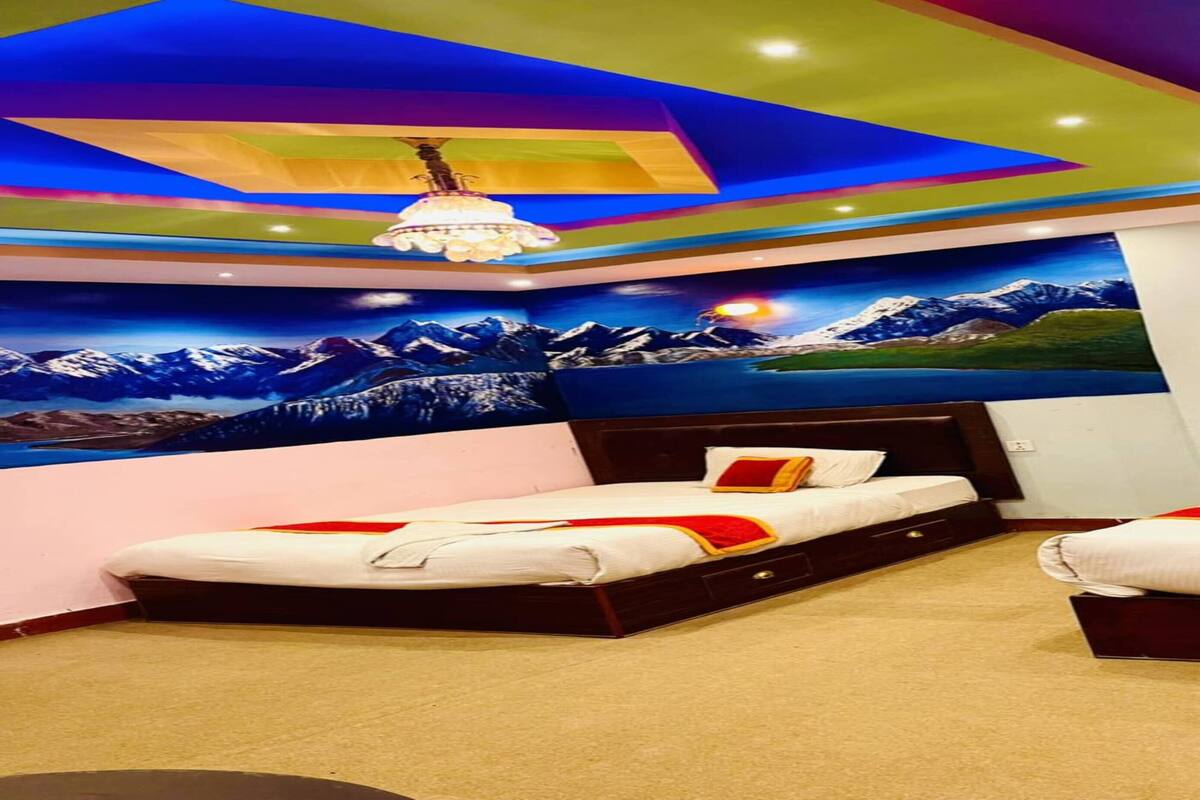 Une chambre d’hôtel avec deux lits, un plafond aux couleurs vives et une fresque représentant un paysage de montagne.