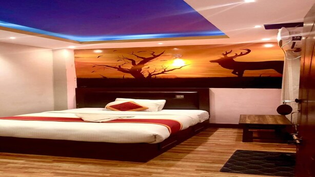 Una habitación de hotel moderna con una cama grande, un cabecero de madera, un mural en el techo con un árbol y ciervos, y una mesita de noche.