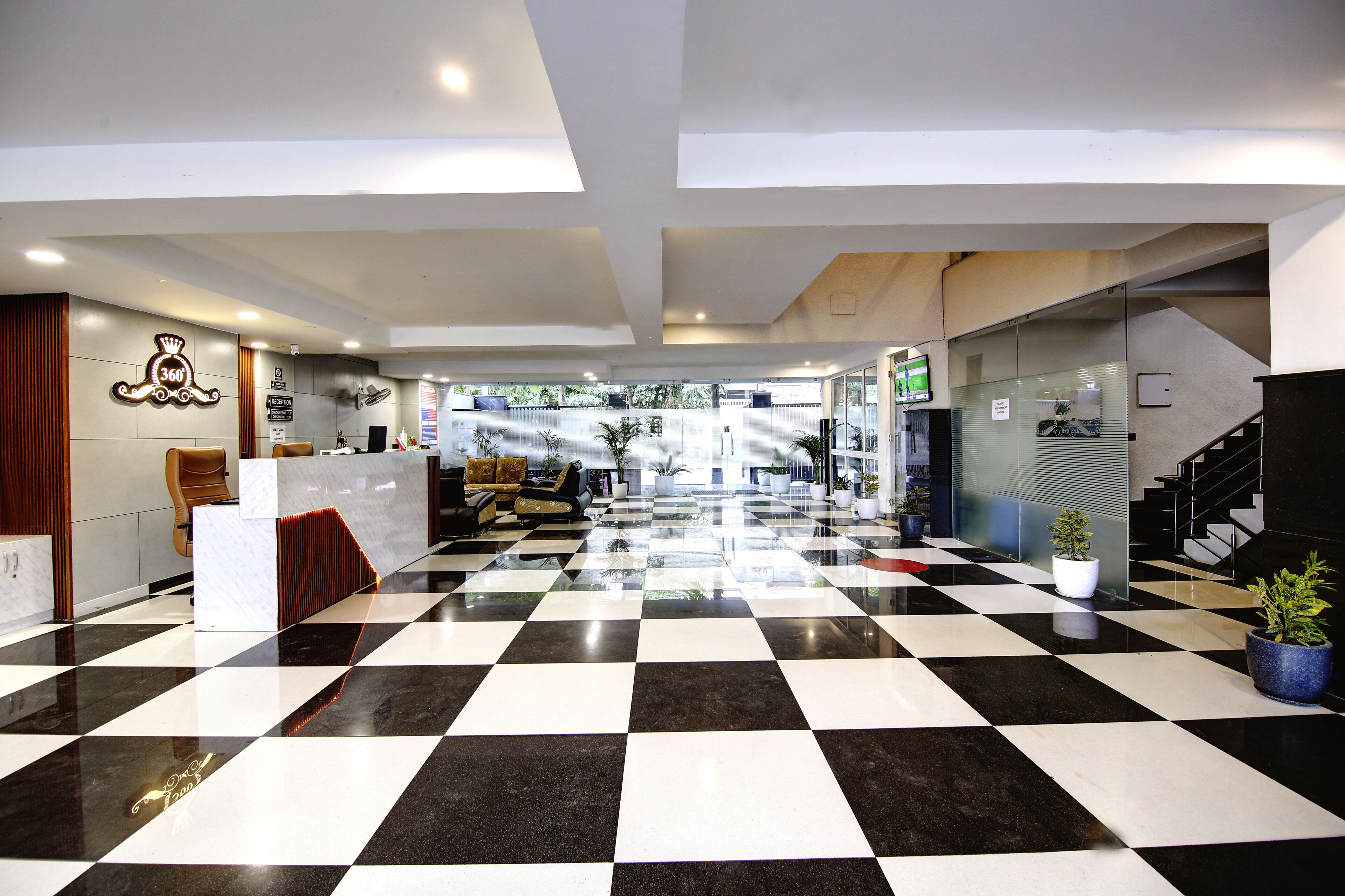 Vestíbulo de hotel con piso a cuadros, mostrador de recepción, zona de estar y una escalera.