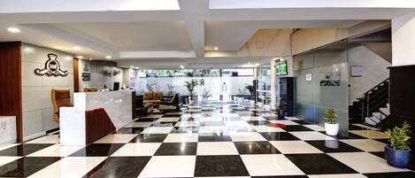 Vestíbulo de hotel con piso a cuadros, mostrador de recepción, zona de estar y una escalera.