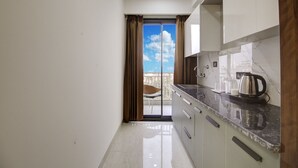 Una cocina moderna con encimera de mármol, un hervidor y vistas a un balcón con una silla.
