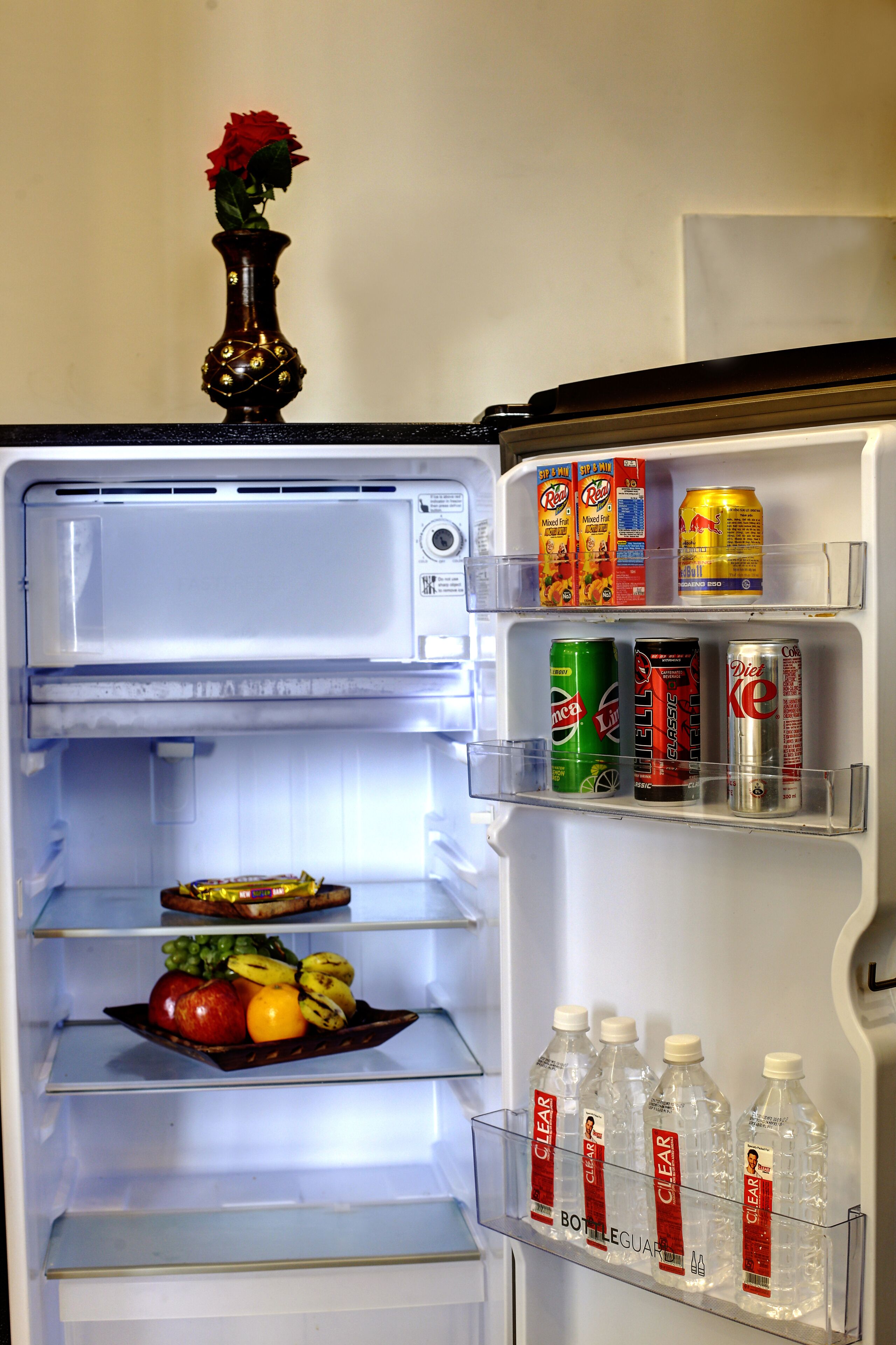 A refrigerator with a vase of flowers on top, various beverages, and a fruit tray.