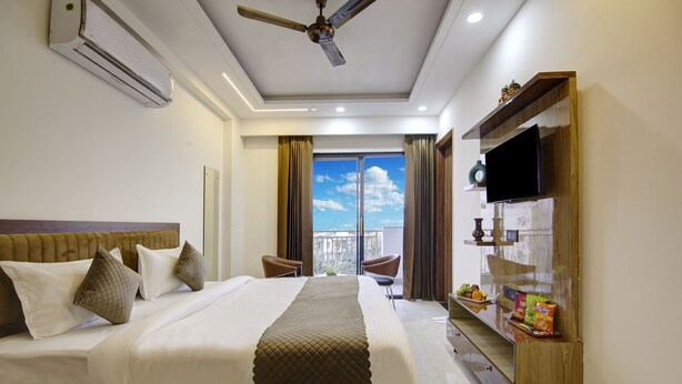Una habitación de hotel con una cama grande, un ventilador de techo, televisión y vista a la ciudad desde la ventana.
