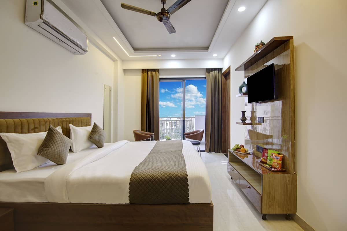 A hotel room with a large bed, a ceiling fan, a TV, and a view of the city through the window.