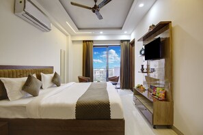 A hotel room with a large bed, a ceiling fan, a TV, and a view of the city through the window. - 360 Degree Hotel (Gurugram)