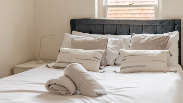 Een net opgemaakt bed met een donker hoofdbord, witte lakens en meerdere kussens.