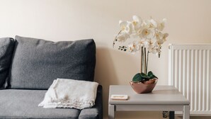 Een grijze bank met een witte plaid en een kleine tafel met een orchidee in pot.