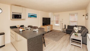 Een moderne woonkamer met een keukenhoek, een flatscreen-televisie en een eettafel.