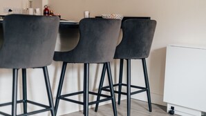 Een moderne keuken met drie grijze barstoelen, een wit aanrecht en een witte kast.