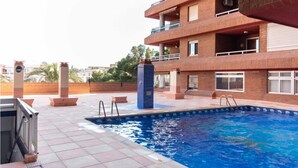 A swimming pool area with a tiled deck, a pool ladder, and a building with multiple balconies in the background.