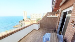 A balcony with a wooden floor, a table, and a view of the sea and buildings.