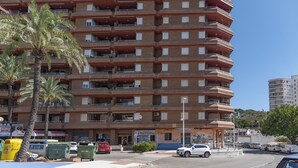 A multi-story residential building with balconies, a street in front, and palm trees.