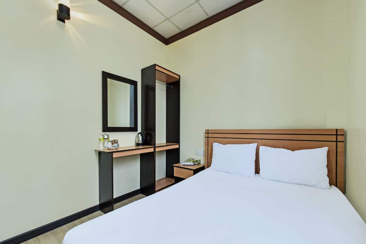 A hotel room with a bed, a nightstand, a mirror, and a small table with a kettle and a bottle.