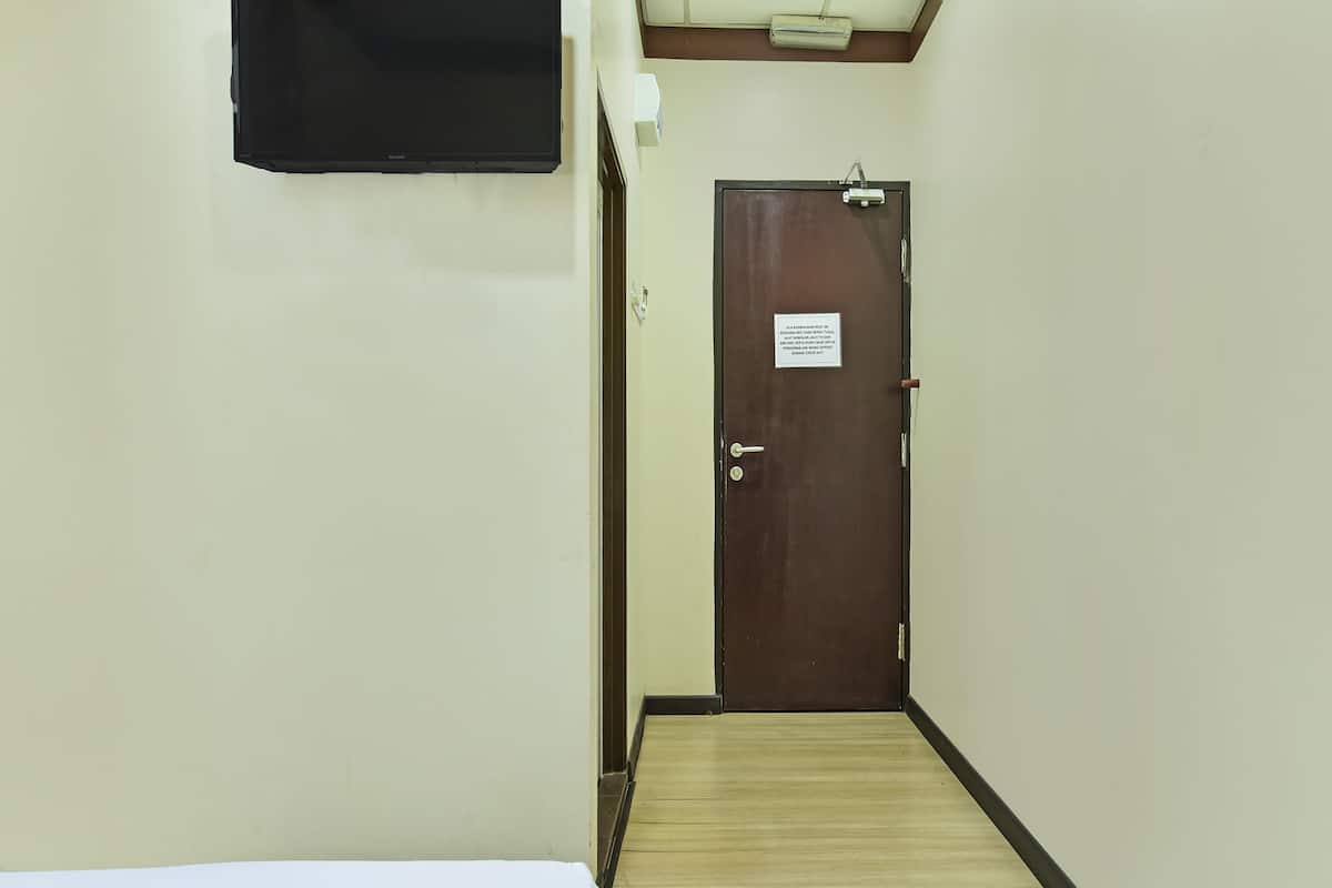 A narrow hallway with a wooden floor, a closed door with a sign, and a bed with white bedding.